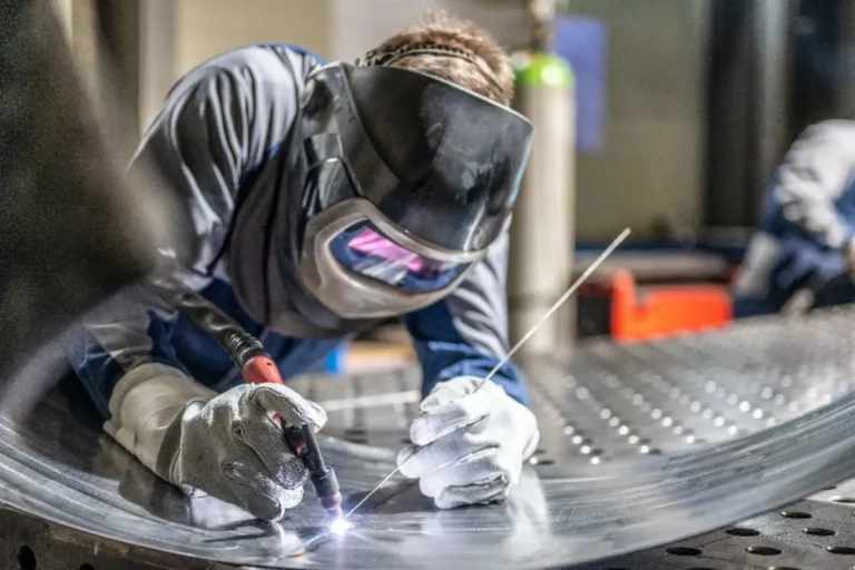 Welder using TIG welding torch to join metal laminate sheets, with sparks visible during the fabrication process.